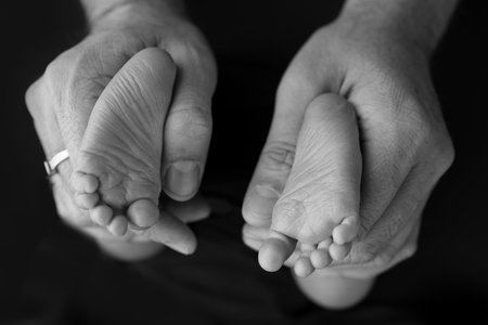 Black and white shade beautiful shape hands of mother, hold tiny newborn baby feet on black background with love, care, family safety and protection, child with premature birth concept or NICU careの写真素材