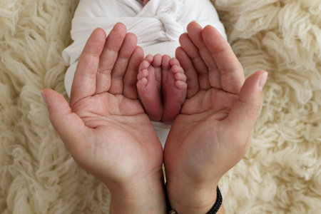 Feet of the newborn on the palms of the parents. The palms of the father and mother are holding the foot of the newborn baby in a white flokati blanket. Photography of a childs toes, heels and feet.の写真素材