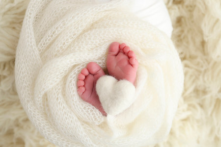 The tiny foot of a newborn baby. Soft feet of a new born in a white wool blanket. Close up of toes, heels and feet of a newborn. Knitted white heart in the legs of a baby. Macro photographyの写真素材