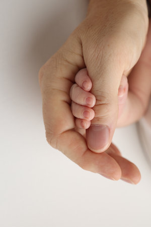 Close-up of a small hand of a child and the hand of mother and father. A newborn baby after birth holds tightly, squeezed the thumb of its parents.の写真素材