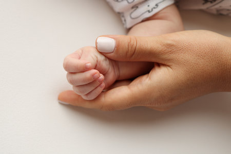 Parents hands hold the fingers of a newborn baby. The hand of a mother and father close-up holds the fist of a newborn baby. Family health and medical care. Professional photo on white backgroundの写真素材