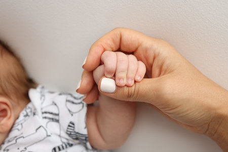 Parents hands hold the fingers of a newborn baby. The hand of a mother and father close-up holds the...