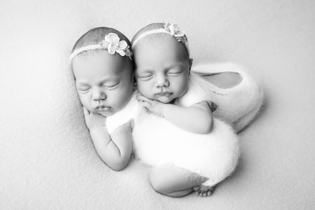 Photo for Tiny newborn twin girls. A newborn twin embraces and sleeps on his sister, Newborn twin girls against a pale blue blanket with white bandages and white delicate woolen bodysuits. Black and white. - Royalty Free Image