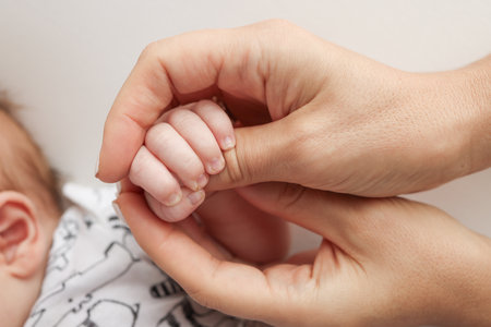 Parents hands hold the fingers of a newborn baby. The hand of a mother and father close-up holds the fist of a newborn baby. Family health and medical care. Professional photo on white backgroundの写真素材
