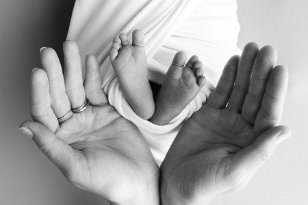 The palms of the parents, father and mother hold the legs, feet of newborn baby.の写真素材