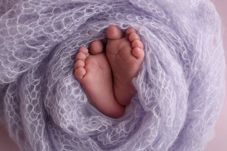 The tiny foot of a newborn baby. Soft feet of a new born in a lilac, purple wool blanket. Close up of toes, heels and feet of a newborn. Macro photography.の写真素材