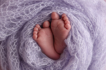 The tiny foot of a newborn baby. Soft feet of a new born in a lilac, purple wool blanket. Close up of toes, heels and feet of a newborn. Macro photography.の写真素材