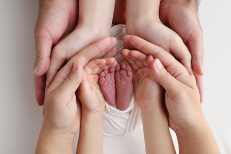 The palms of the father, the mother are holding the foot of the newborn baby in a white blanket.