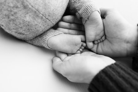 The palms of the father, the mother are holding the foot of the newborn baby.