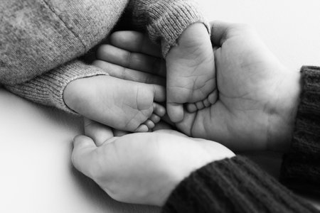 The palms of the father, the mother are holding the foot of the newborn baby.