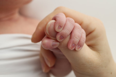 Close-up little hand of child and palm of mother and father. The newborn baby has a firm grip on the parents finger after birth. A newborn holds on to moms, dads finger.の写真素材
