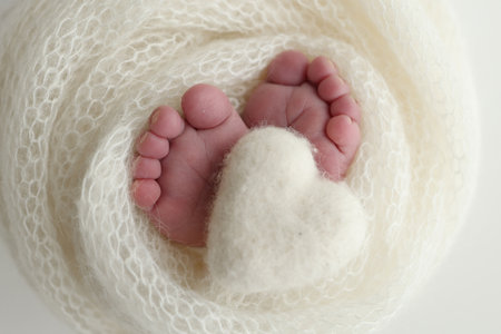 The tiny foot of a newborn baby. Soft feet of a new born in a white wool blanket. Close up of toes, heels and feet of a newborn. Knitted white heart in the legs of a baby. Macro photographyの写真素材