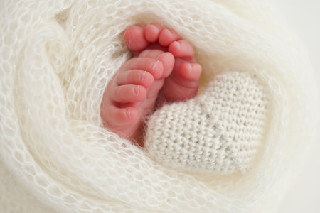 The tiny foot of a newborn baby. Soft feet of a new born in a white wool blanket. Close up of toes,...