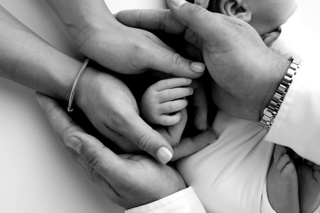 Small hand of a newborn baby with tiny fingers, head, nose and ear of a newborn. Palm hand of parents, father and mother of a newborn. Studio macro black and white photography.の写真素材