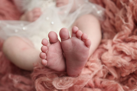 The tiny foot of a newborn. Soft feet of a newborn in a pink red flakatti. Close up of toes, heels and feet of a newborn baby.Openwork white dress. Studio Macro photography. Womans happiness.の写真素材