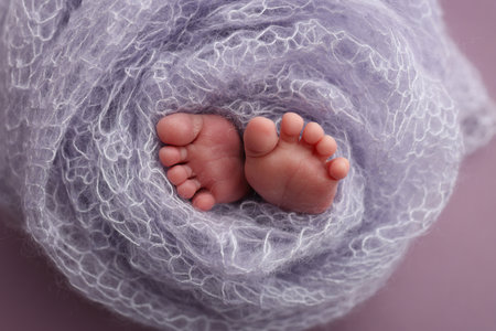 The tiny foot of a newborn. Soft feet of a newborn in a purple lilac woolen blanket. Close up of toes, heels and feet of a newborn baby. Studio Macro photography. Womans happiness.の写真素材
