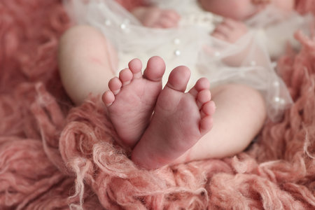 The tiny foot of a newborn. Soft feet of a newborn in a pink red flakatti. Close up of toes, heels and feet of a newborn baby.Openwork white dress. Studio Macro photography. Womans happiness.の写真素材