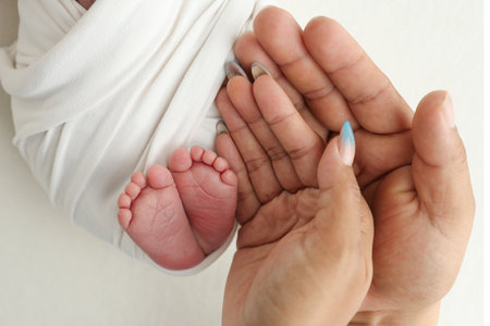 The palms of the parents. A father and mother hold the feet of a newborn child in a white blanket on a white background.. The feet of a newborn in the hands of parents. Photo of foot, heels and toesの写真素材