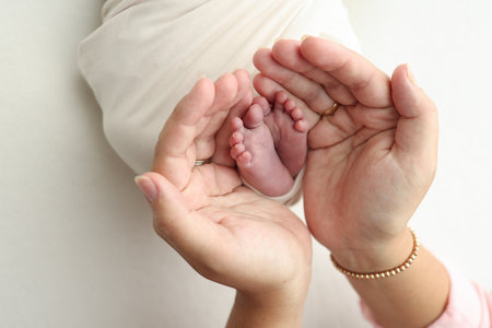 The palms of the parents. A father and mother hold the feet of a newborn child in a white blanket on a white background.. The feet of a newborn in the hands of parents. Photo of foot, heels and toesの写真素材