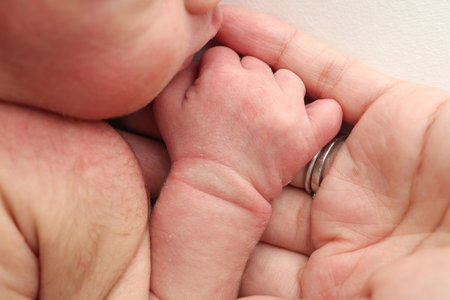 Close-up little hand of child and palm of mother and father. The newborn baby has a firm grip on the parents finger after birth. A newborn holds on to moms, dads finger.の写真素材