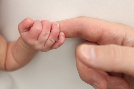 The newborn baby has a firm grip on the parents finger after birth. Close-up little hand of child and palm of mother and father. Parenting, childcare and healthcare concept.の写真素材