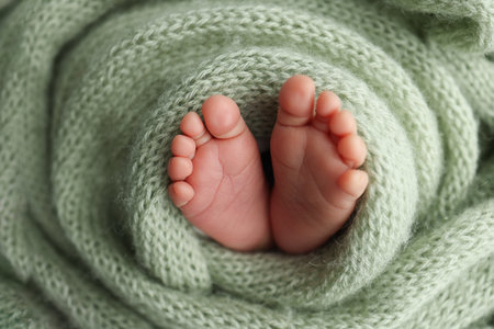 The tiny foot of a newborn. Soft feet of a newborn in a olive green woolen blanket. Close up of toes, heels and feet of a newborn baby. Studio Macro photography. Womans happiness.の写真素材