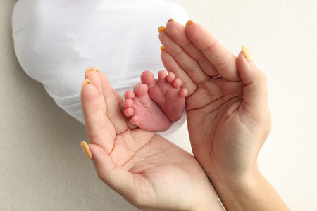 The palms of the parents. A father and mother hold the feet of a newborn child in a white blanket on...