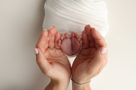 The palms of the parents. A father and mother hold the feet of a newborn child in a white blanket on a white background.. The feet of a newborn in the hands of parents. Photo of foot, heels and toesの写真素材