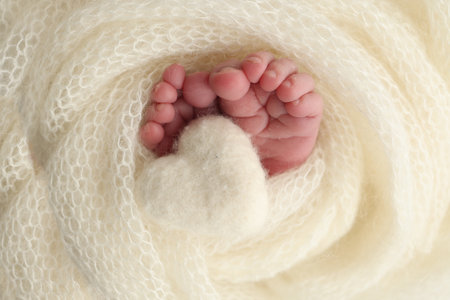 The tiny foot of a newborn baby. Soft feet of a new born in a white wool blanket. Close up of toes, heels and feet of a newborn. Knitted white heart in the legs of a baby. Macro photography.の写真素材