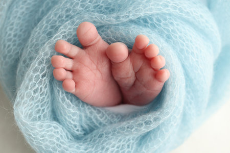 Close-up of tiny, cute, bare toes, heels and feet of a newborn girl, boy. Baby foot on blue soft coverlet, blanket. Detail of a newborn baby legs. Macro horizontal professional studio photo.の写真素材
