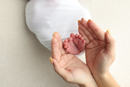 A father and mother hold the feet of a newborn child in a white blanket on a white background.の写真素材