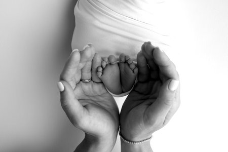 The palms of the parents. A father and mother hold the feet of a newborn child in a blanket. The feet of a newborn in the hands of parents. Black and white Photo of foot, heels and toesの写真素材