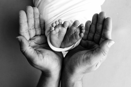 Black and white shade beautiful shape hands of mother, hold tiny newborn baby feet on black background with love, care, family safety and protection, child with premature birth concept or NICU careの写真素材