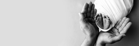 Black and white shade beautiful shape hands of mother, hold tiny newborn baby feet on black background with love, care, family safety and protection, child with premature birth concept. Banner.の写真素材