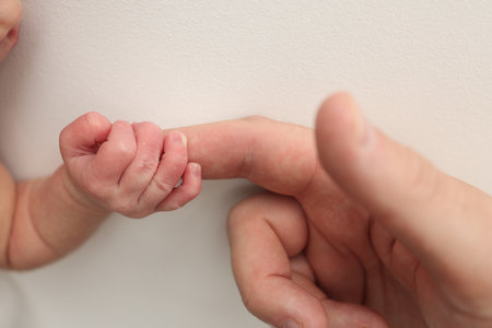 Close-up little hand of child and palm of mother and father. The newborn baby has a firm grip on the parents finger after birth. A newborn holds on to moms, dads finger.の写真素材