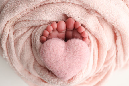 Soft feet of a new born in a wool pink blanket. Closeup of toes, heels and feet of a newborn. Knitted pink heart in the legs of baby. Macro studio photography The tiny foot of a newborn baby.の写真素材