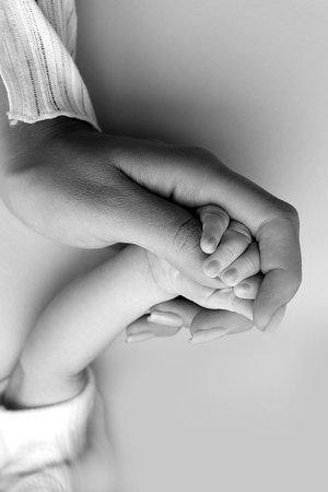 Close-up little hand of child and palm of mother and father. The newborn baby has a firm grip on the parents finger after birth. A newborn holds on to moms, dads finger. Black and white photo.の写真素材