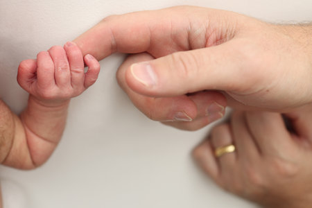 Close-up little hand of child and palm of mother and father. The newborn baby has a firm grip on the parents finger after birth. A newborn holds on to moms, dads finger.の写真素材