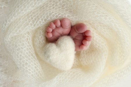 Soft feet of a new born in a white wool blanket. Close up of toes, heels and feet of a newborn. Knitted white heart in the legs of a baby. Macro photography.The tiny foot of a newborn babyの写真素材