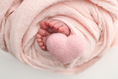 Soft feet of a new born in a wool pink blanket. Closeup of toes, heels and feet of a newborn. Knitted pink heart in the legs of baby. Macro studio photography The tiny foot of a newborn baby.の写真素材