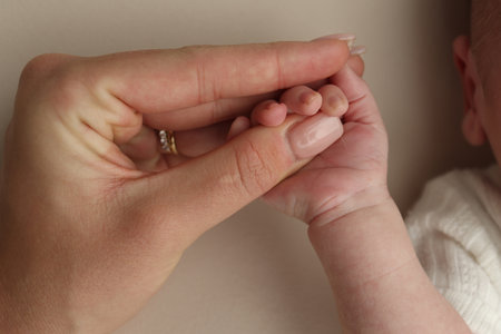 Close-up little hand of child and palm of mother and father. The newborn baby has a firm grip on the parents finger after birth. A newborn holds on to moms, dads finger.の写真素材