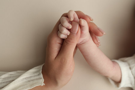 Close-up little hand of child and palm of mother and father. The newborn baby has a firm grip on the parents finger after birth. A newborn holds on to moms, dads finger.の写真素材