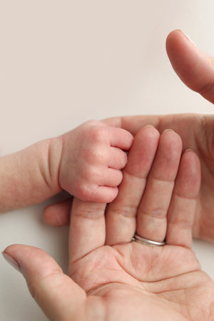 Close-up little hand of child and palm of mother and father. The newborn baby has a firm grip on the parents finger after birth. A newborn holds on to moms, dads finger.の写真素材