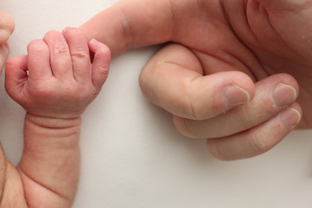 Close-up little hand of child and palm of mother and father. The newborn baby has a firm grip on the parents finger after birth. A newborn holds on to moms, dads finger.の写真素材