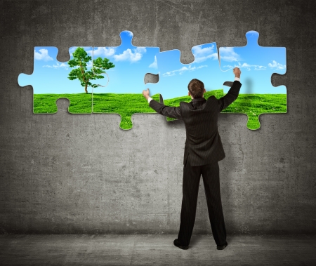Businessman making a puzzle on the wall with picture of nature Businessman making a puzzle on the wall with picture of nature