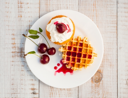 Cakes with cherry on a white plate on wooden boardsの写真素材