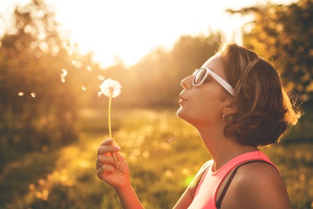 Happy young woman blowing on a dandelion in park の写真素材