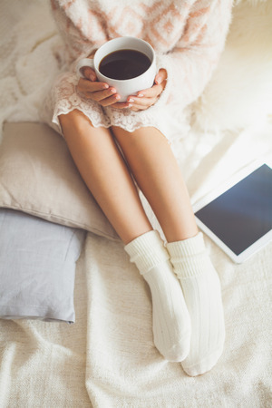 Soft photo of woman on the bed with tablet and cup of coffee in hands, top view pointの写真素材