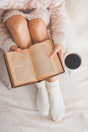 Soft photo of woman on the bed with old book and cup of coffee, top view point