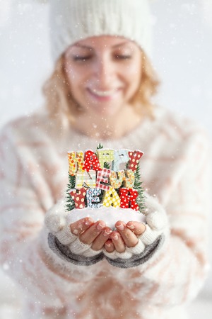 Young woman in mittens holding snow in her hands with colorful text Happy new year. Unusual christmas conceptの写真素材